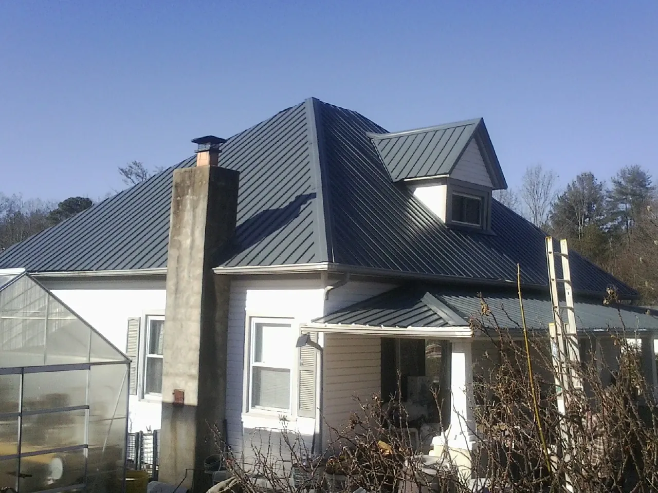 Dark blue standing seam metal roof on a white farmhouse with dormer — Slate & Tile Roof Repair by Roofing Brothers in Chelmsford