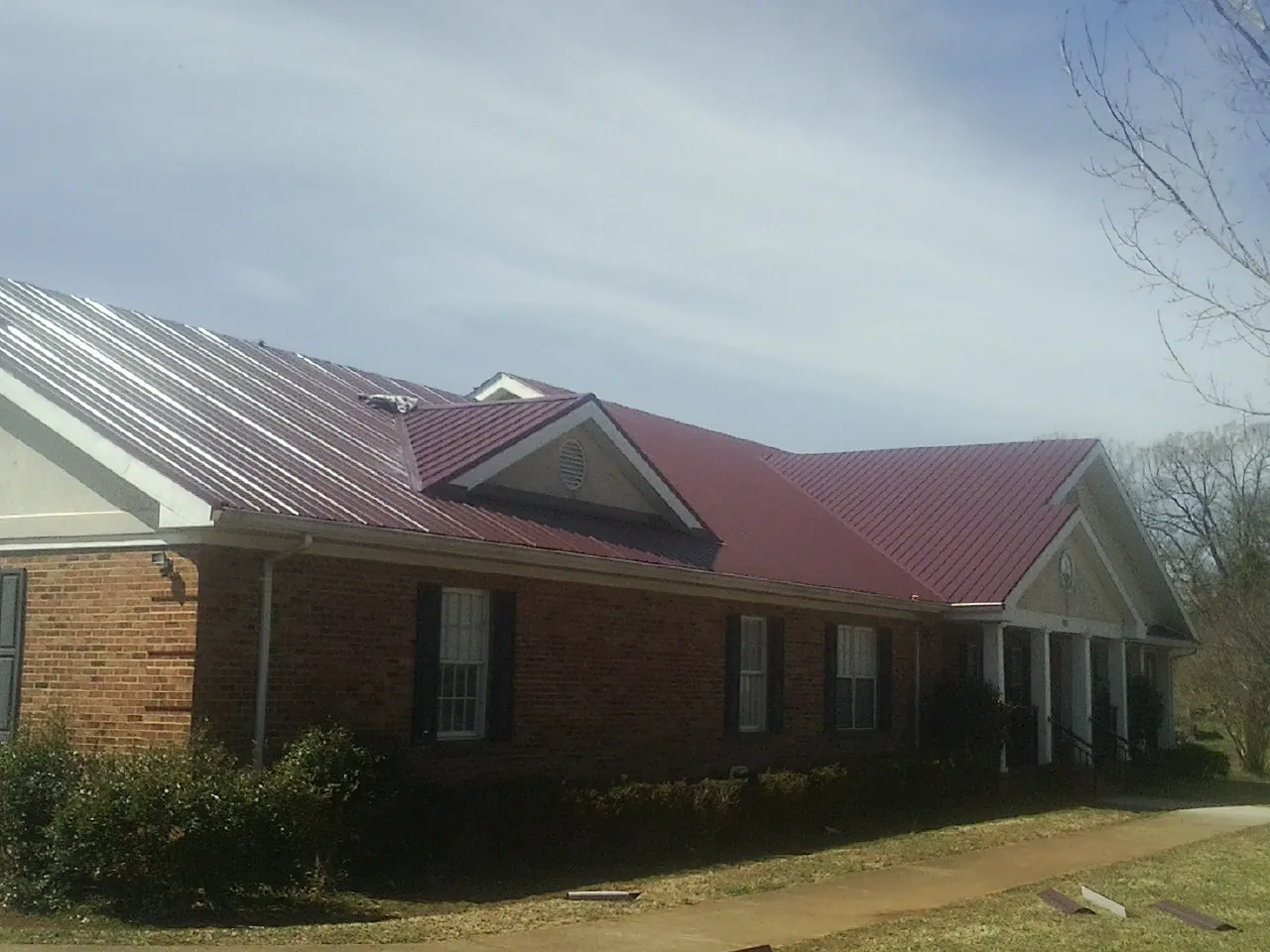 Red metal roof with gabled entries on a long brick building, from a Hail Damage Roof Repair job in Chelmsford