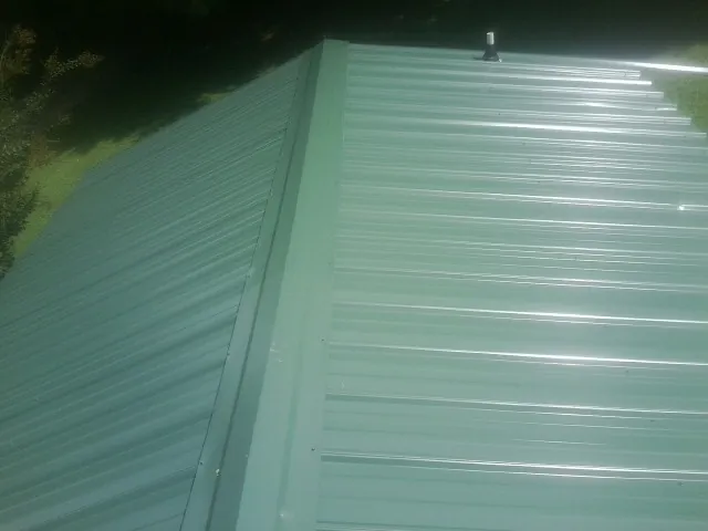 New green metal panels meeting at the ridge of a roof — Flat Roof Repair work by our crew in Chelmsford