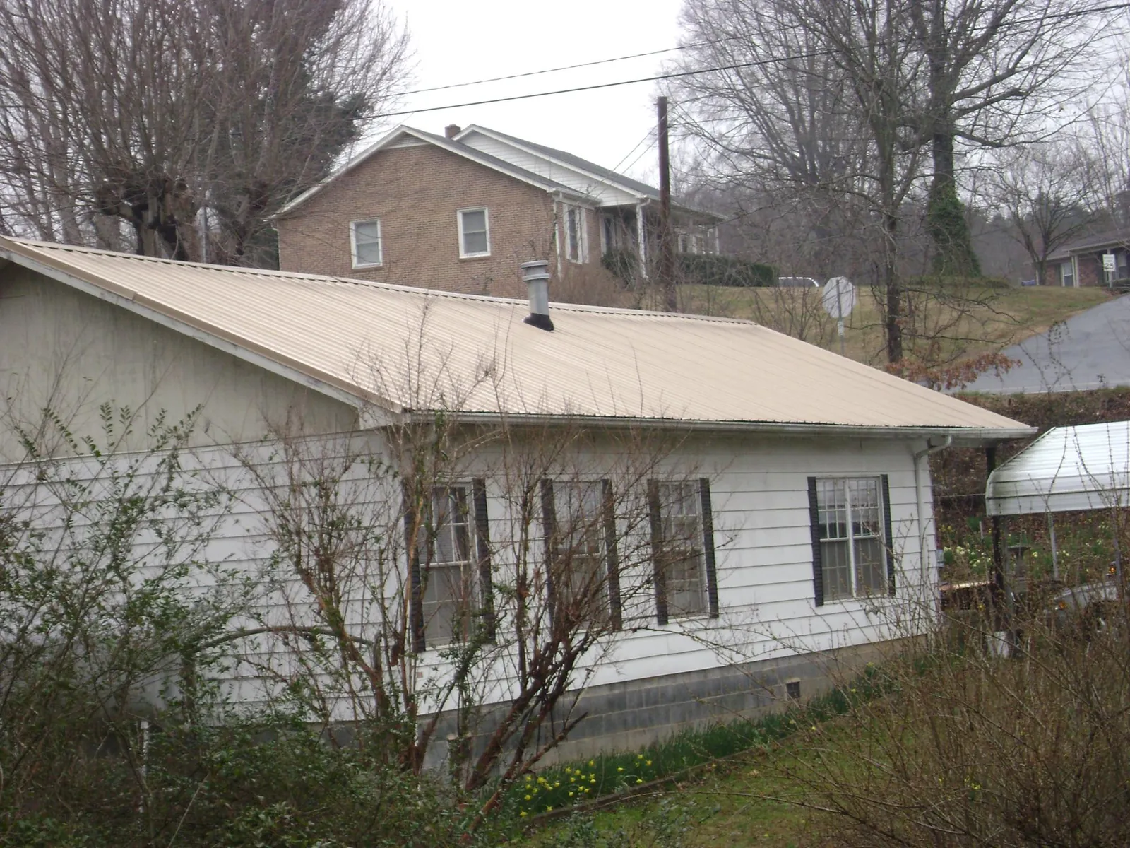 Tan metal roof on a white sided house set into a hillside — Commercial Roofing by Roofing Brothers in Chelmsford