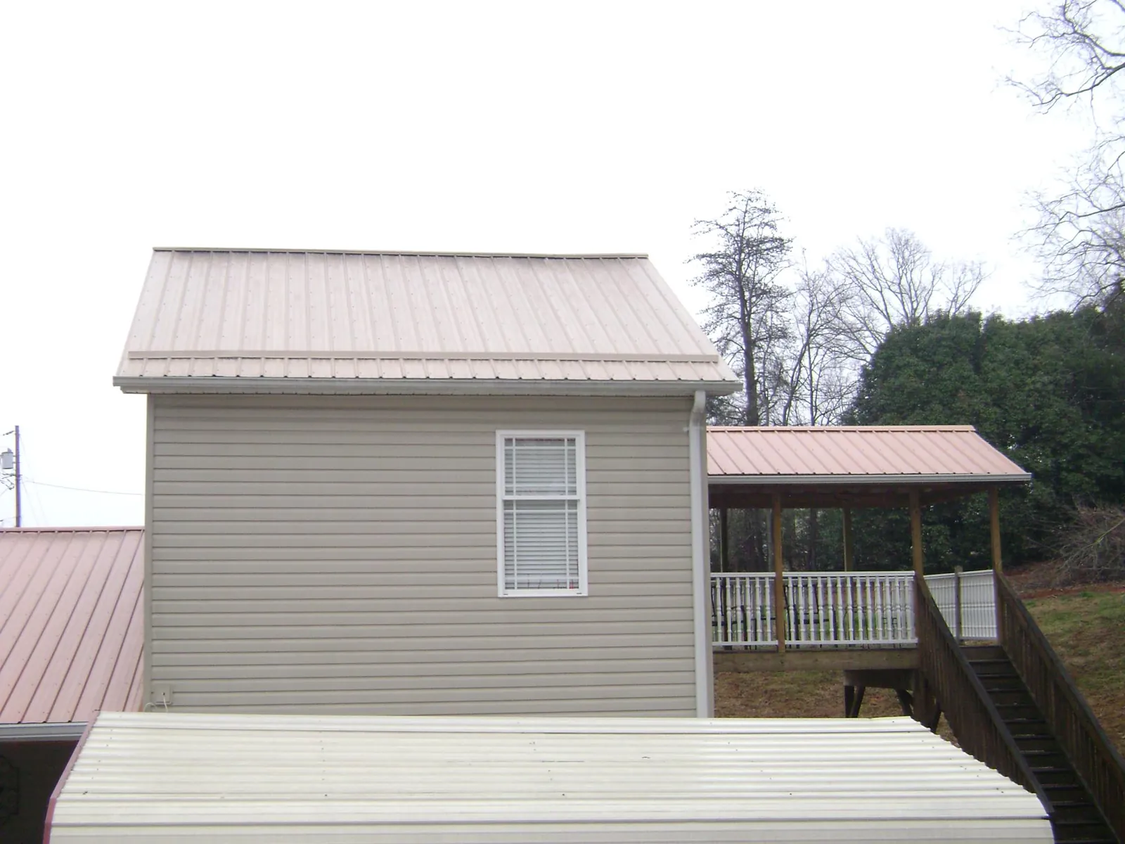 Tan metal roofs on a two story addition and attached porch, from a Roof Replacement job in Chelmsford